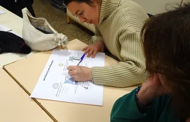 Une adulte écrit sur une feuille intitulée "Speed boat du jardin pédagogique".