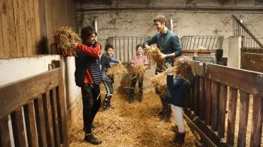 Un groupe d'enfants et leur animateur dans la grange se lancent de la paille 