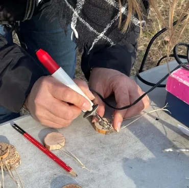 Gros plan sur les mains d'une adulte qui dessine au pyrograveur sur un petit rondin de bois.