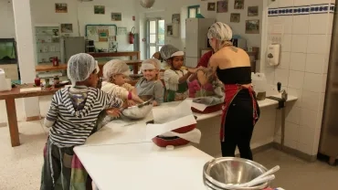 Six enfants avec leurs charlottes sur la tête pétrissent la pâte avec leur animatrice pour faire les focaccia dans la cuisine pédagogique
