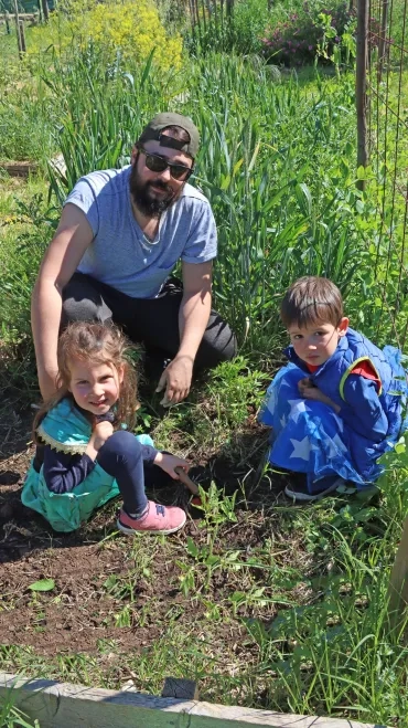 Deux enfants et leur animateur sont devant des plants de tomate au jardin