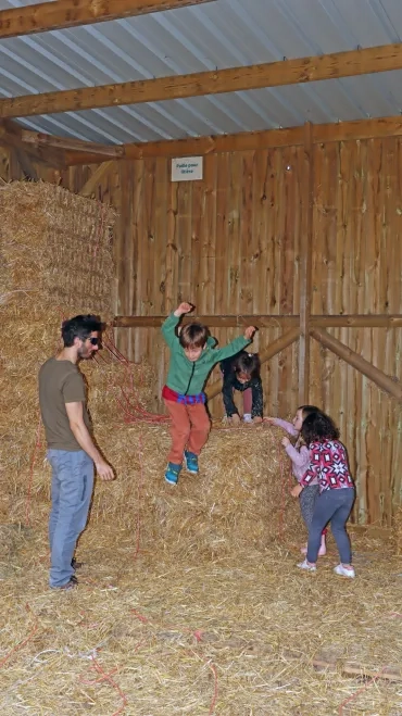 des enfants, surveillés par un animateur sautent d'une botte de paille