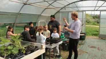 Un animateur montrant aux sept enfants de son groupe comment semer des graines en pots dans la serre