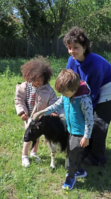 Deux enfants et leur animatrice caressent le bouc
