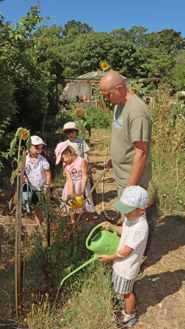 un groupe d'enfants et leur animateur arrosent le jardin