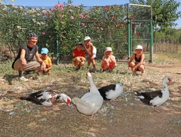 Un groupe d'enfants et leur animatrice sont derrère des canards de Barbarie