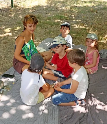 Un groupe d'enfants et leur animatrice sont assis sur un plaid avec un livre