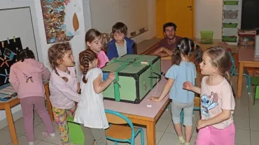 Un groupe d'enfants et leur animateur tournent autour d'une grosse boîte en bois