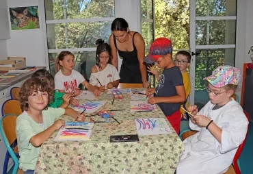 Un groupe d'enfants et leur animatrice peignent des morceaux de bois