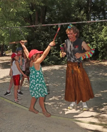 un enfant marche sur un fil tendu devant son animateur déguisé en dinosaure.