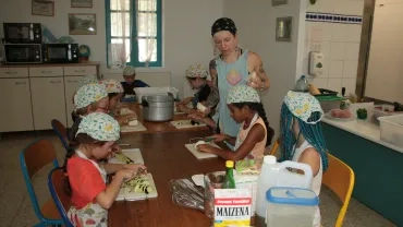Habillés de leur tabliers et charlottes une animatrice distribue des morceaux d'aubergine aux enfants pendant que d'autres découpent les légumes