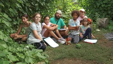Un groupe d'enfants et leur animateur sont assis sous le feuillage