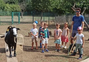 Un groupe d'enfant et un animateur observent une chèvre sur une planche surélevée