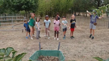 Un groupe d'enfant et une animatrice jettent des crottins dans une brouette