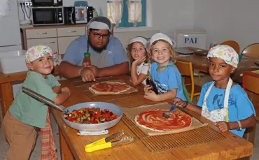 Un groupe d'enfants et un animateur déposent des légumes sur une pizza