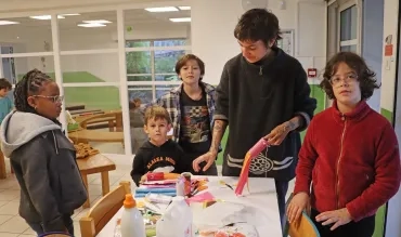 un groupe d'enfants et leur animatrice collent des bandelettes sur des rouleaux de papier toilette
