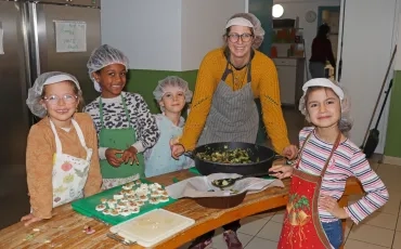 un groupe d'enfants et leur animatrice sont en cuisine avec des ingrédients