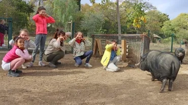 un groupe d'enfants et leur animatrice font des gestes devant un cochon