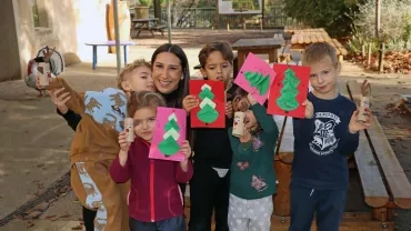 un groupe d'enfants et leur animatrice montrent des cartes en papier avec des sapins