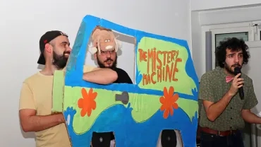 deux animateurs sont derrière un camision en carton et un autre parle dans un micro