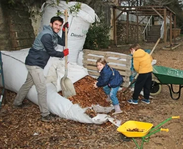 deux enfant et leur animateur mettent des copeaux de bois dans un brouette