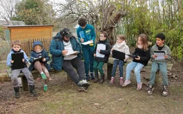 un groupe d'enfants et leur animateur sont assis sur des bancs avec des plaquettes et des feuilles de papiers