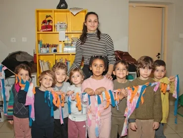 un groupe d'enfants et leur animatrice posent devant des lambeaux de tissus