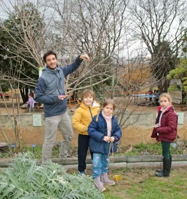 un groupe d'enfants et leur animateur posent dans un jardin devant un arbre sans feuille