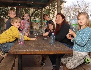 un groupe d'enfants et leur animatrice montrent des bouteilles en plastique coupées en deux