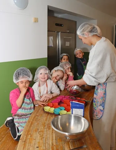 un groupe d'enfants et leur animatrice sont en cuisine avec des petits moules colorés