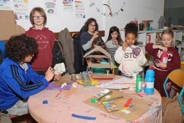 un groupe d'enfants et leur animateur peignent, collent, coupent du carton