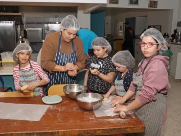 Un groupe d'enfants et leur animatrice en cuisine malaxent de la pâte
