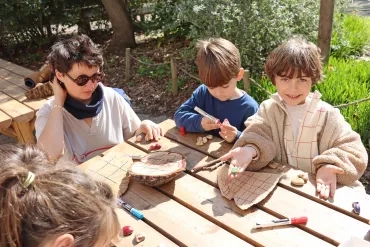 Un groupe d'enfants et leur animatrice colorient des tranches de bois