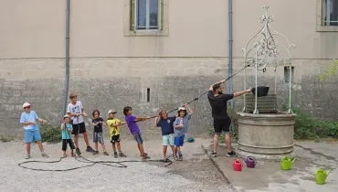 un groupe d'enfants et leur animateur tirent sur la corde du puits