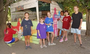 un groupe d'enfants et leur animatrice peignent une cabane