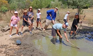 un groupe d'enfants et leur animateur posent avec eds pelles dans un trou plein d'eau