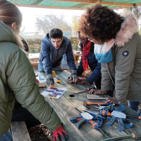 Plusieurs adultes et un animateur sont penchés sur une table contenant quelques outils