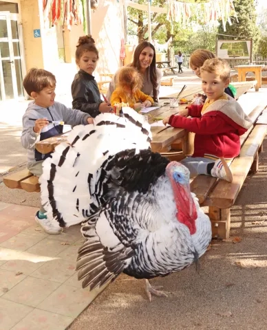 un groupe d'enfants et leur animatrice sont installés à une table avec un dindon devant
