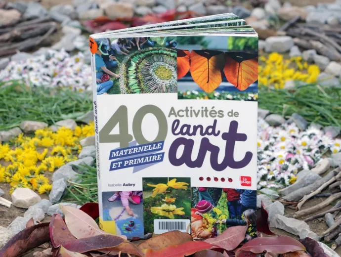 Le livre 40 activités de land art est exposé entouré d'une oeuvre de land art composée de pierres, de branchages, de fleurs et feuilles