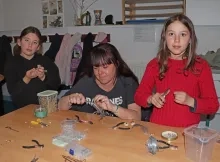 Deux enfants et leur animatrice fabrique des boucles d'oreilles avec des plumes