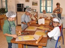 un groupe d'enfants et leur animatrice sont en cuisine avec des charlottes et tabliers en train d'étaler de la pâte