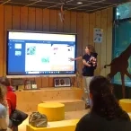 Une animatrice présente un outil pédagogique projeté sur un écran, des adultes sont assis devant 