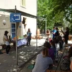 Trois adultes parlent en face d'un groupe d'adultes en extérieur 