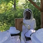 un groupe d'enfants et leur animatrice avec des tenues d'apiculteurs observent un cadre de ruche
