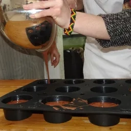 une personne verse la pâte d'un gateau au chocolat dans des moules 